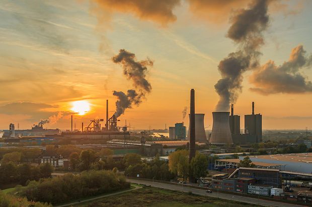 Sonnenuntergang über großer Industrieanlage mit zahlreichen dampfenden und rauchenden Schornsteinen